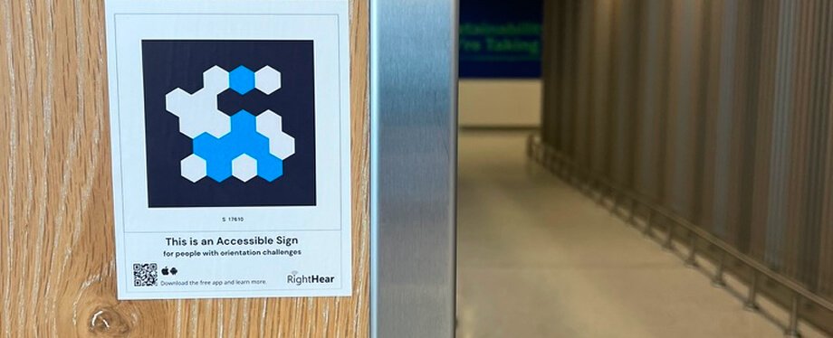A RightHear accessibility sign with a blue hexagon logo mounted on a wooden door near a building entrance